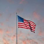 Drapeau des États-Unis flottant au vent sous un ciel de coucher de soleil teinté de rose, pour la célébration du 4 juillet au Tiara Miramar.