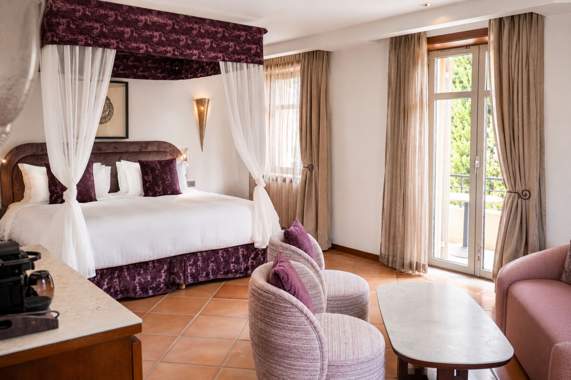 Chambre prune avec lit à baldaquin, coin salon et fauteuils, vue jardin, hôtel 5 étoiles Le Yaktsa Théoule-sur-Mer